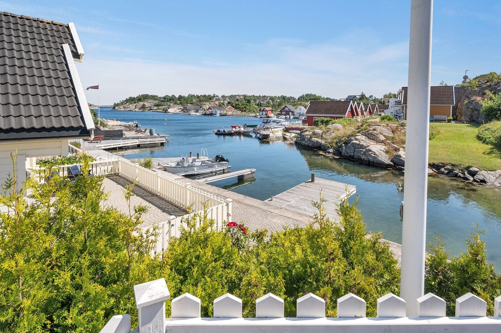 Sørlandsidyll med hvitmalt stakittgjerde, flaggstang og utsikt over sjærgården. Galleribilde