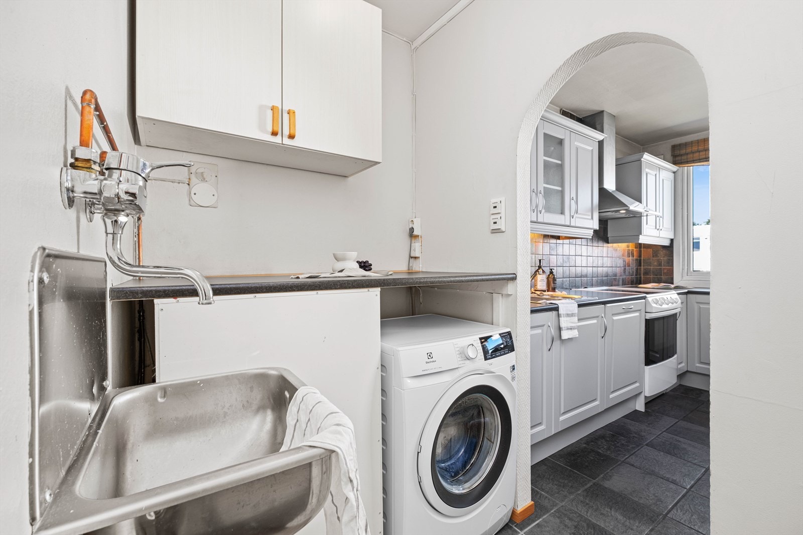 Mellom kjøkkenet og entreen er det en mellomgang innredet med skap, arbeidsbenk, skyllekum og opplegg for vaskemaskin. Galleribilde