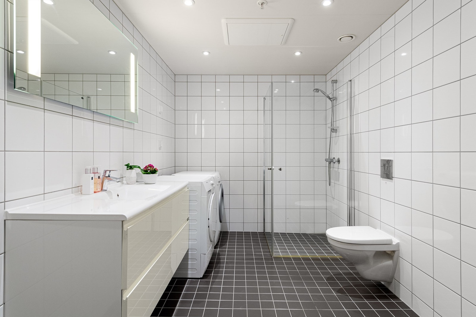 Bad har vegghengt servant og toalett, foldbare dusjdører i glass og opplegg til vaskemaskin. Galleribilde