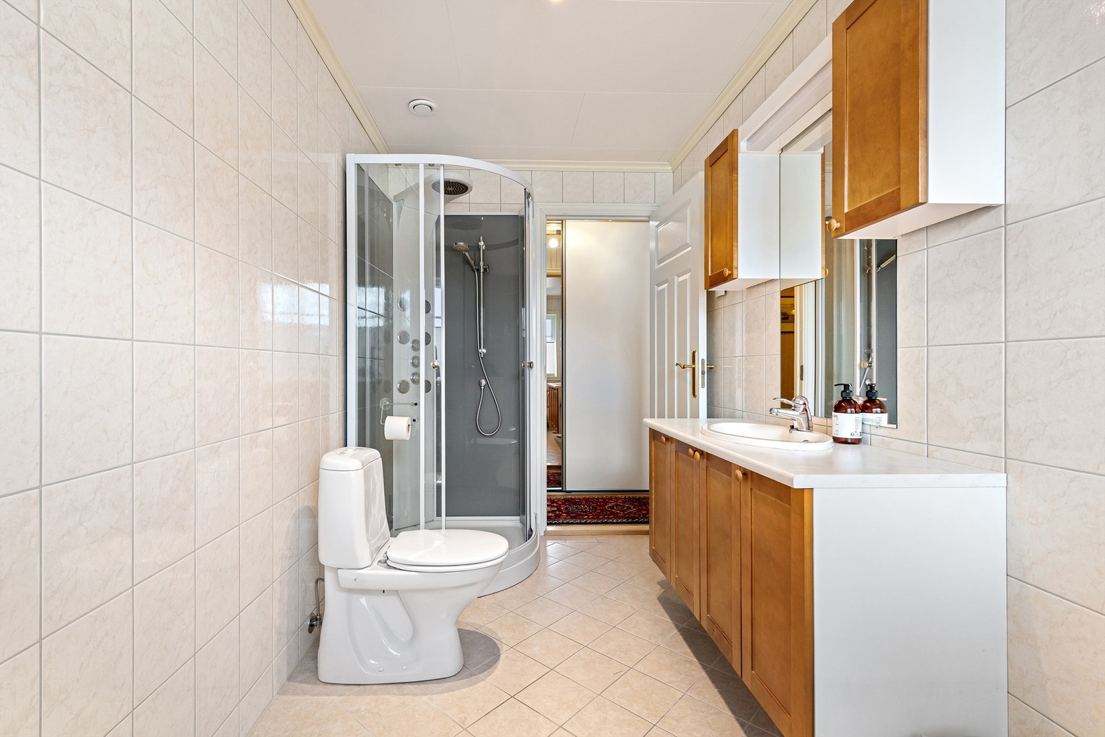 Badet har innredning med ovenpåliggende servant med ett-greps armatur. Speil med overlys og skap over servant. Gulvstående toalett. Dusjkabinett. Galleribilde