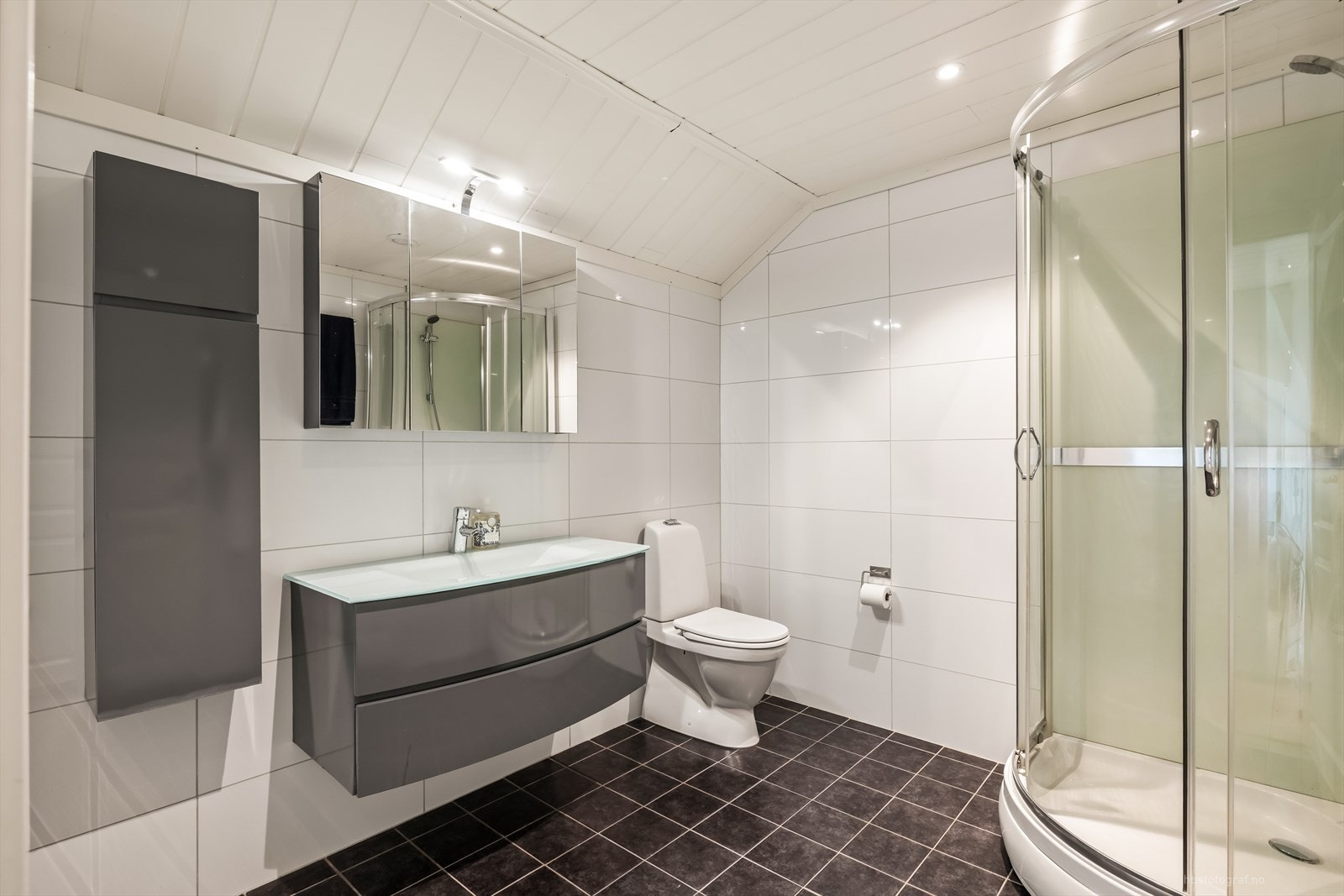 Stilrent bad i loftsetasjen. Badet er innredet med lyse baderomsfliser og mørkere fliser på gulv. Galleribilde