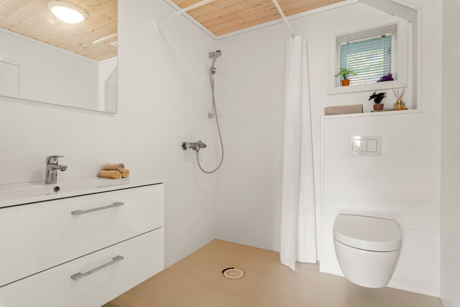 Bad i 1. etasje med hvit vegghengt baderomsinnredning og toalett, samt dusjhjørne med forheng Galleribilde