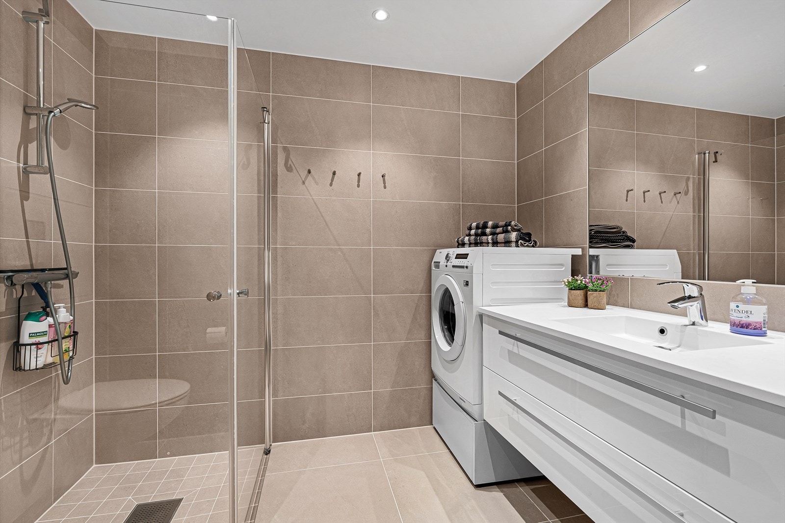 Badet er delikat og lekkert helfliset med gulvvarme. Det inneholder en dusjnisje med innfellbare dusjdører, vegghengt toalett, samt baderomsinnredning med speil over. Galleribilde