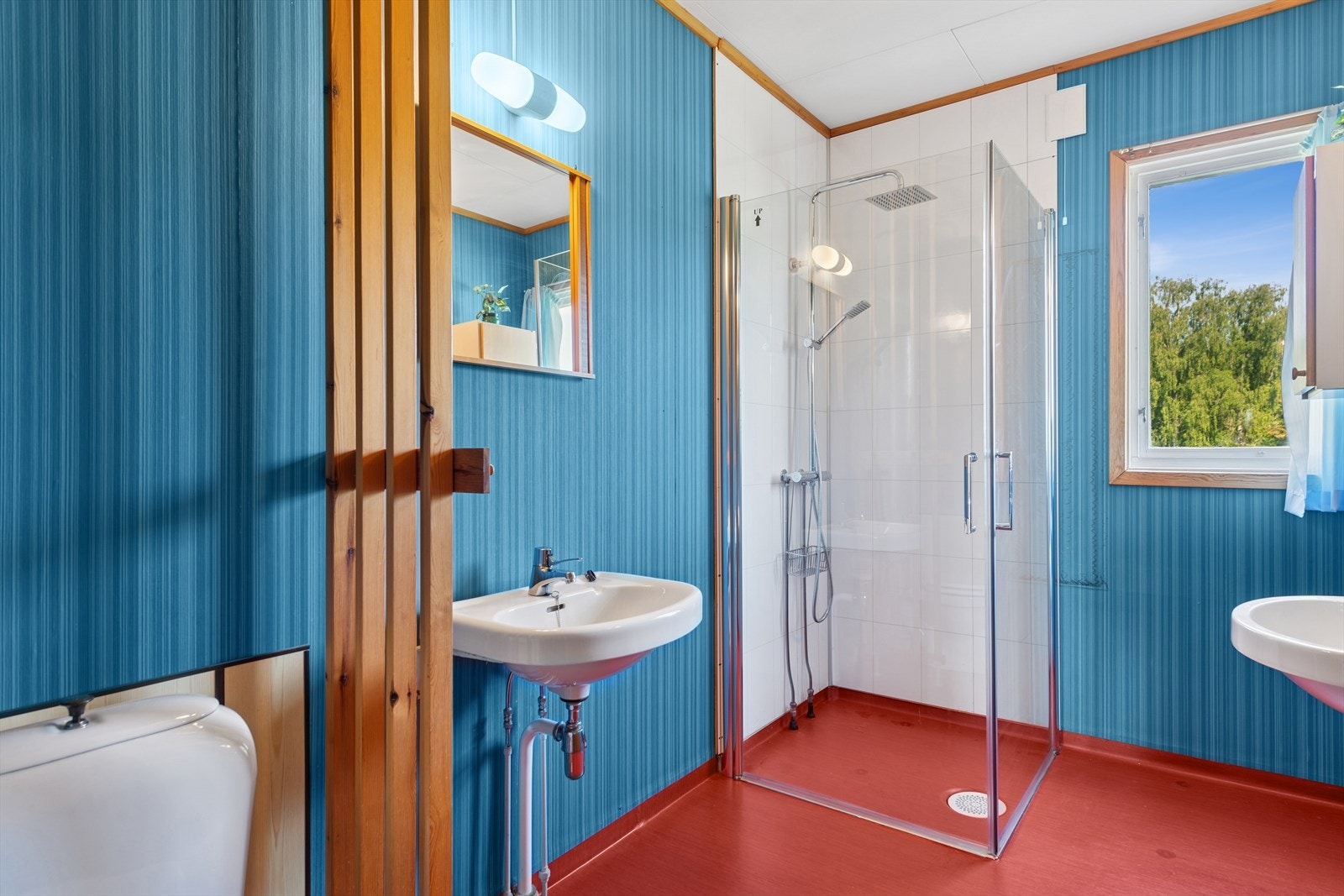 Badet i første etasje er fra 1973 da boligen ble tilbygget, og har våtromsbelegg på gulvet og tapetserte plater på veggene. Det er våtromsplater på veggene i dusjsonen. Galleribilde