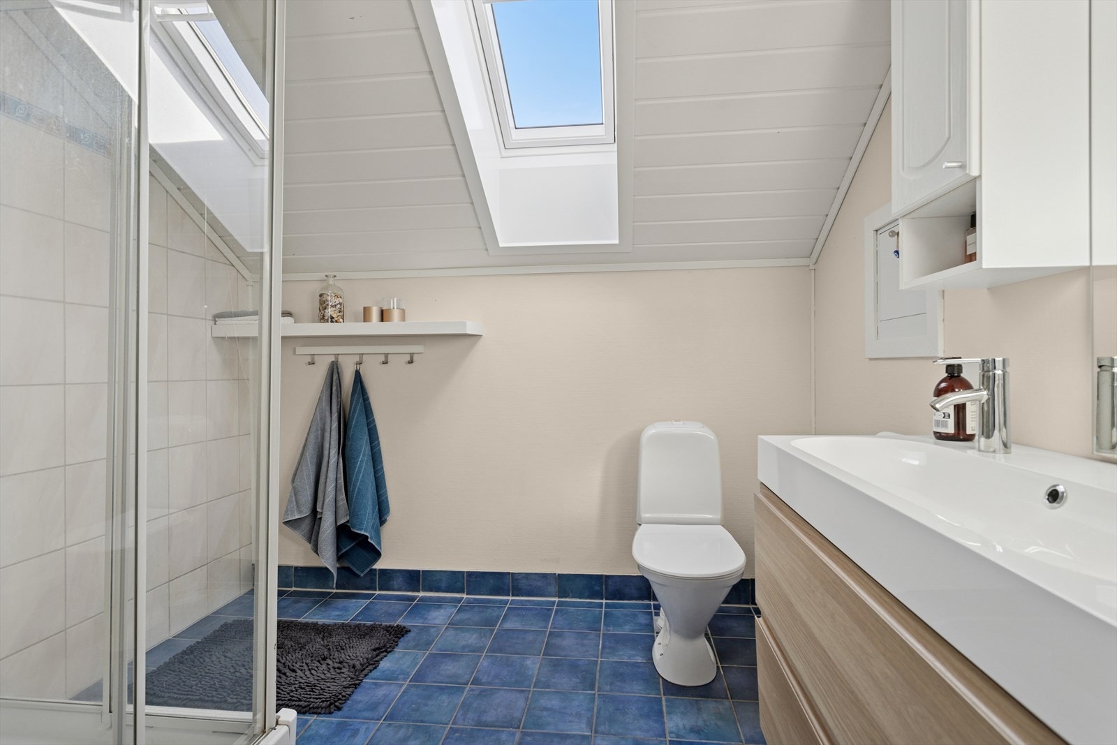 Badet er utstyrt med dusjkabinett, gulvmontert toalett og innredning med servant. Galleribilde