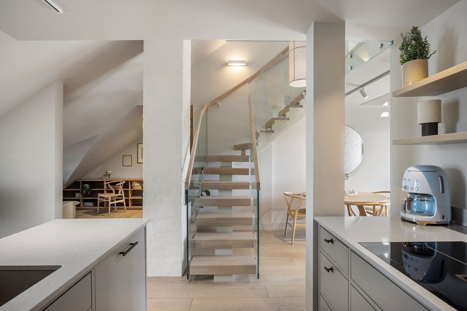 Fra leiligheten fører en åpen tretrapp med eiketrinn og rekkverk i glass med håndløpere i eik opp til loftet. Galleribilde