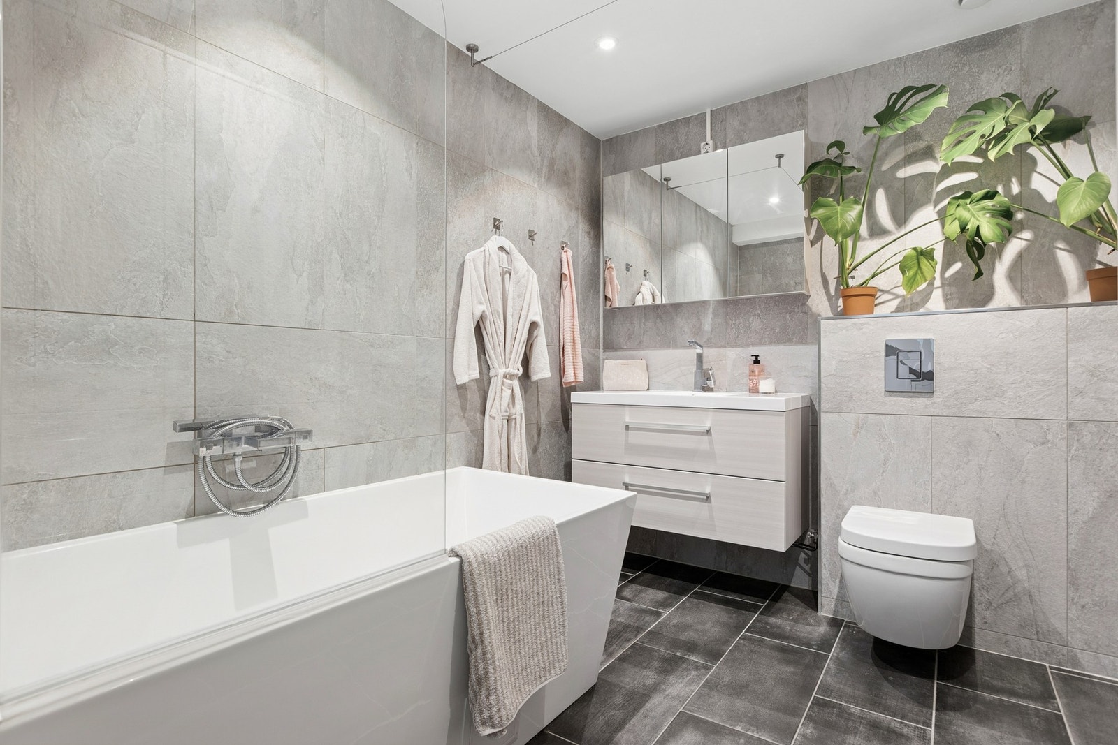 Delikat og flislagt baderom med gulvvarme, en moderne baderomsinnredning og badekar. Galleribilde