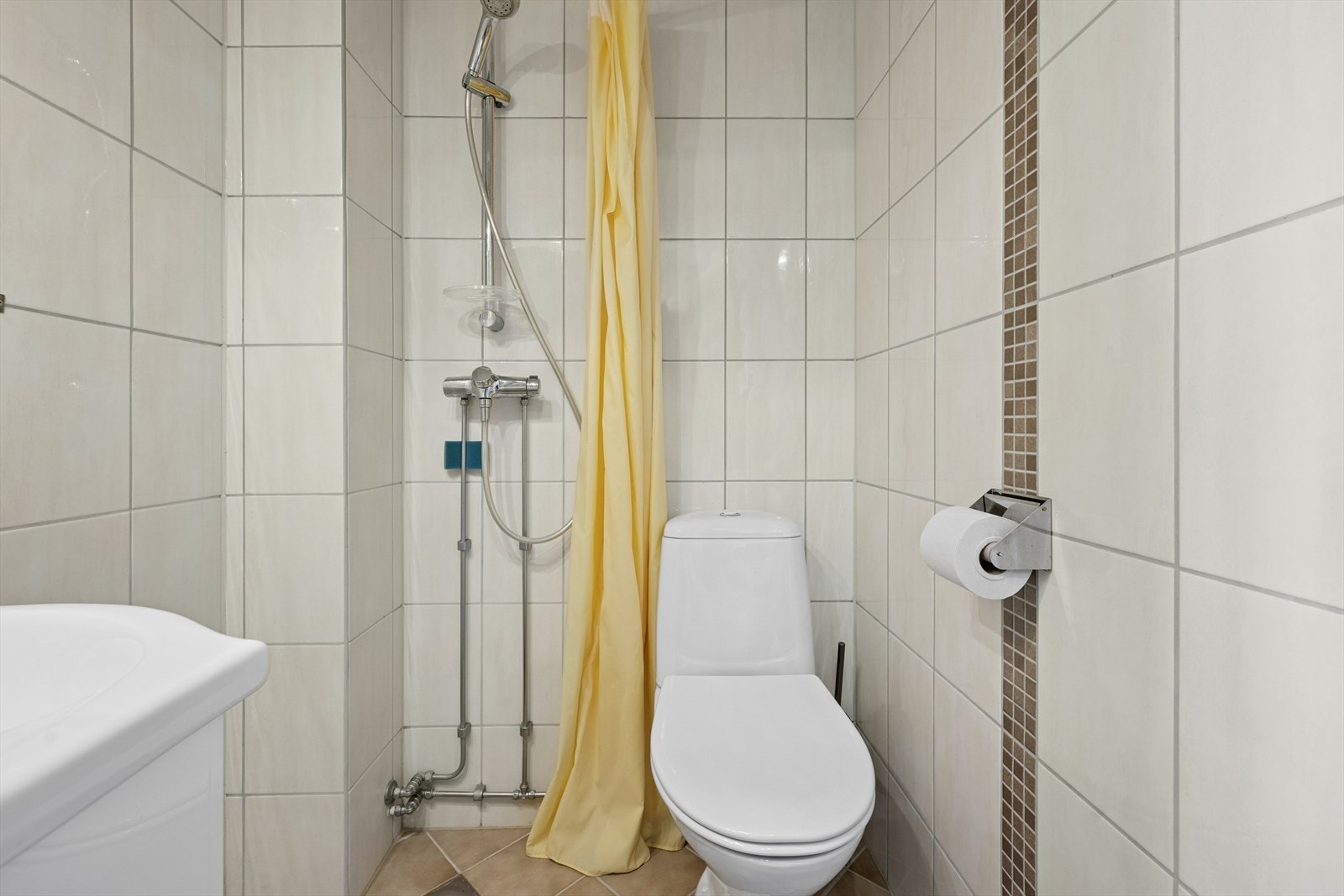 Badet er utstyrt med dusjhjørne med dusjforheng og gulvstående toalett. Galleribilde