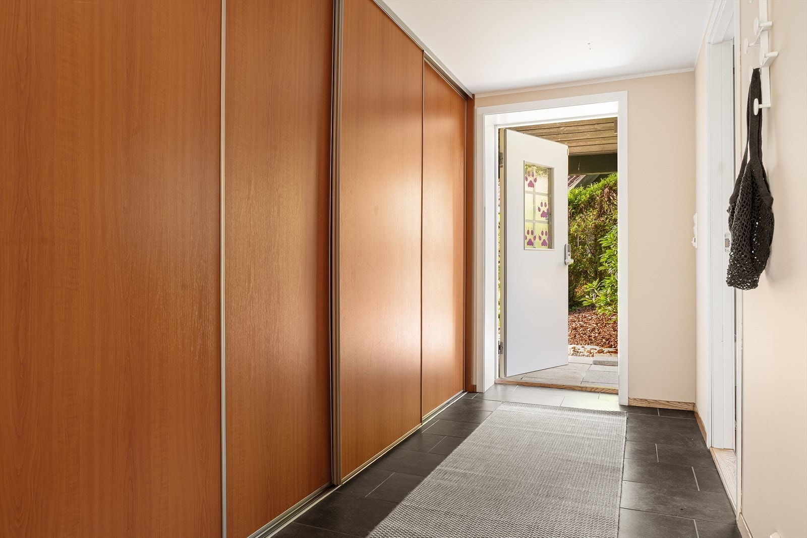 Lys entré med fliser på gulv og stor skyvedørsgarderobe for yttertøy og sko. Galleribilde