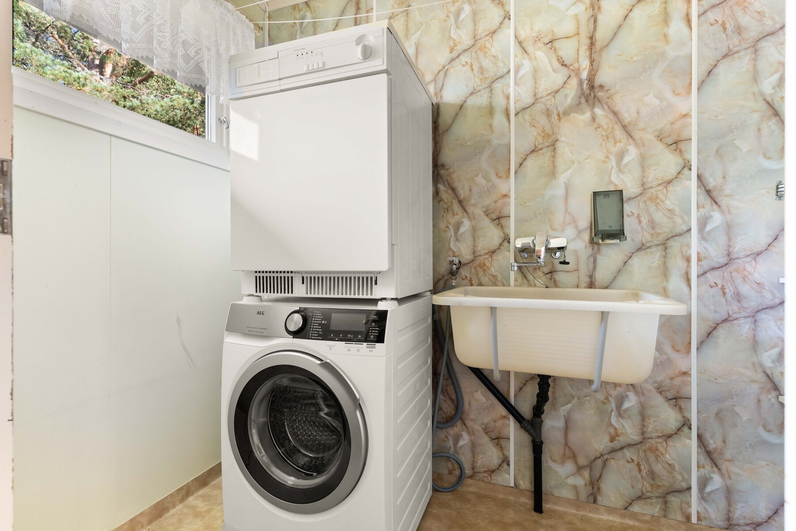 Vaskerommet fra byggeåret har belegg på gulv, malte plater og baderomsplater på veggene. Vegghengt utslagsvask og opplegg for vaskemaskin gjør det enkelt å ta hånd om klær. Galleribilde