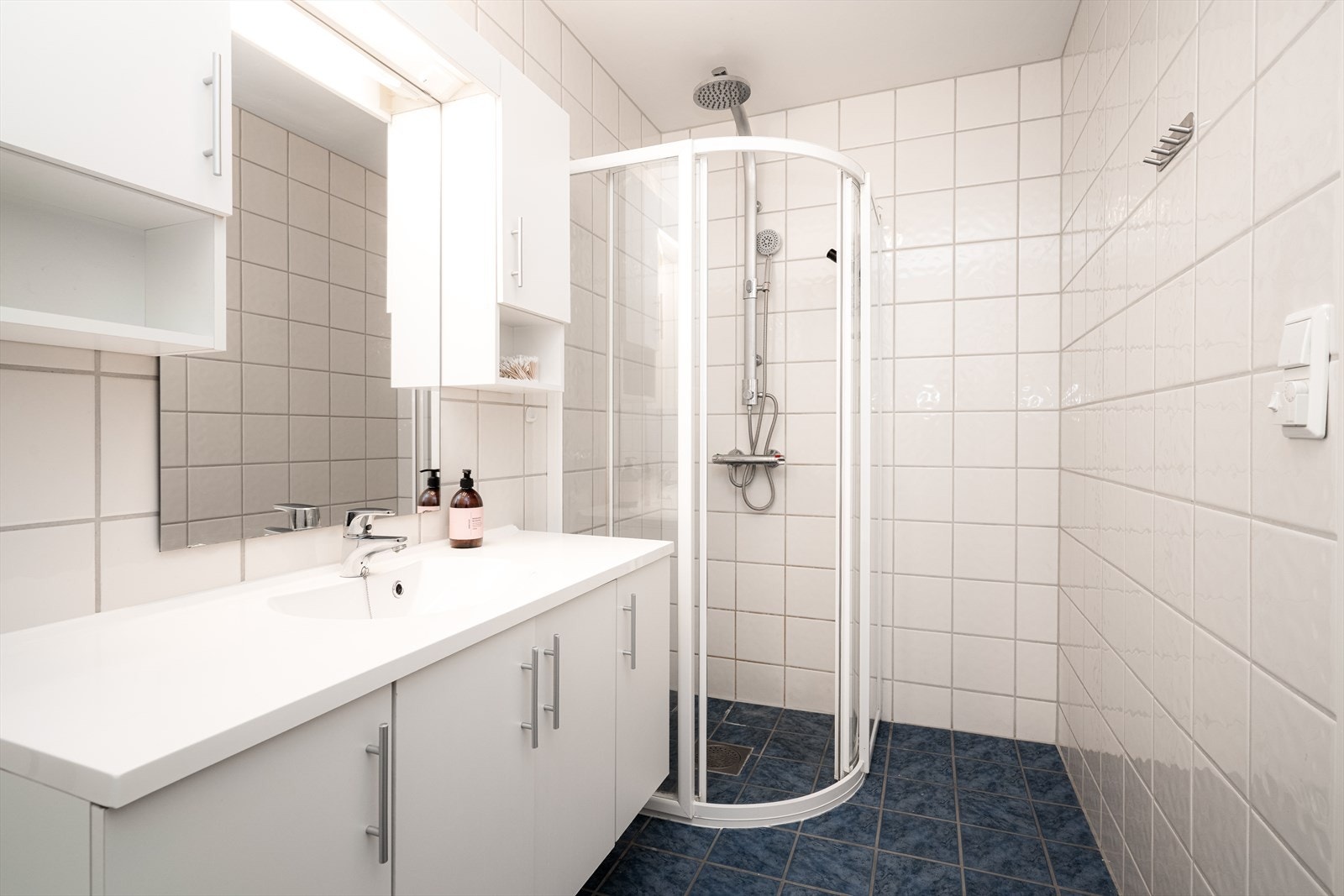 Lyst, flislagt baderom fra byggeår. Badet har elektriske varmekabler, toalett og dusjhjørne med skyvedører. Galleribilde