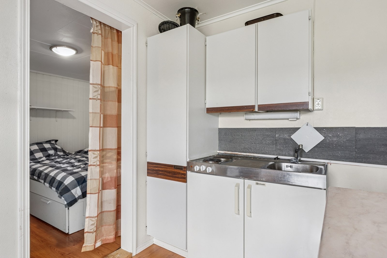 Hybelkjøkkenet har eldre innredning med glatte fronter, som gir et enkelt og funksjonelt uttrykk. Galleribilde