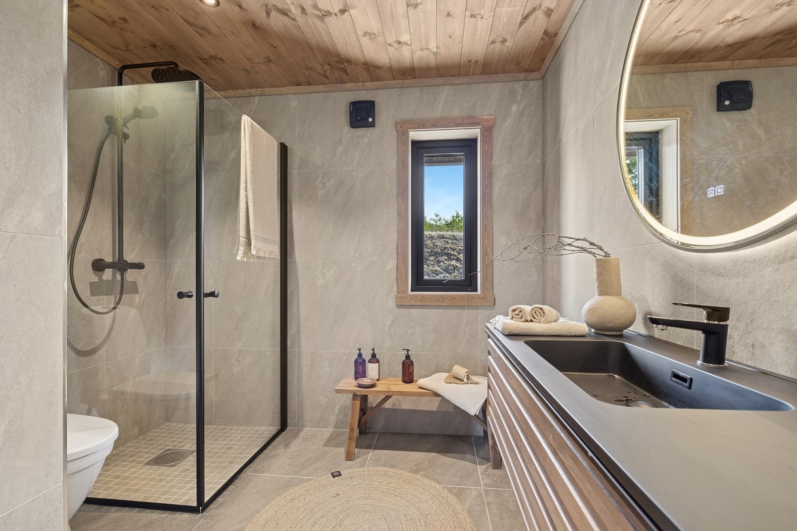 Lekkert flislagt bad med sorte detaljer som servantinnredning, blandebatterier og dusjvegger. Galleribilde