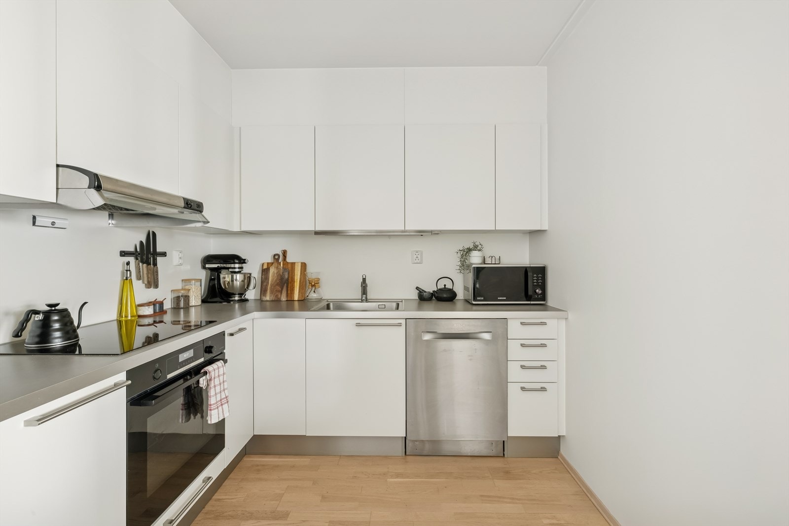 Lyst og nøytralt kjøkken med helslette fronter og takhøye skap. Galleribilde