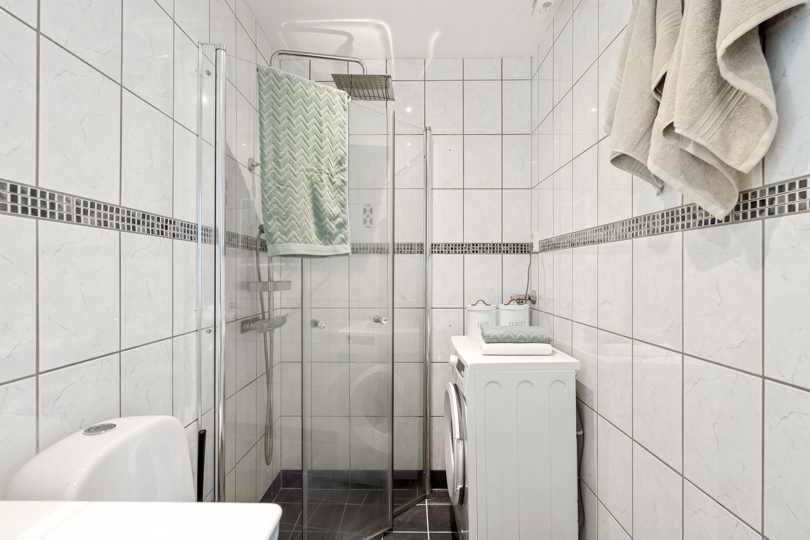 Badet har vegghengte dusjdører i glass og opplegg for vaskemaskin. Galleribilde