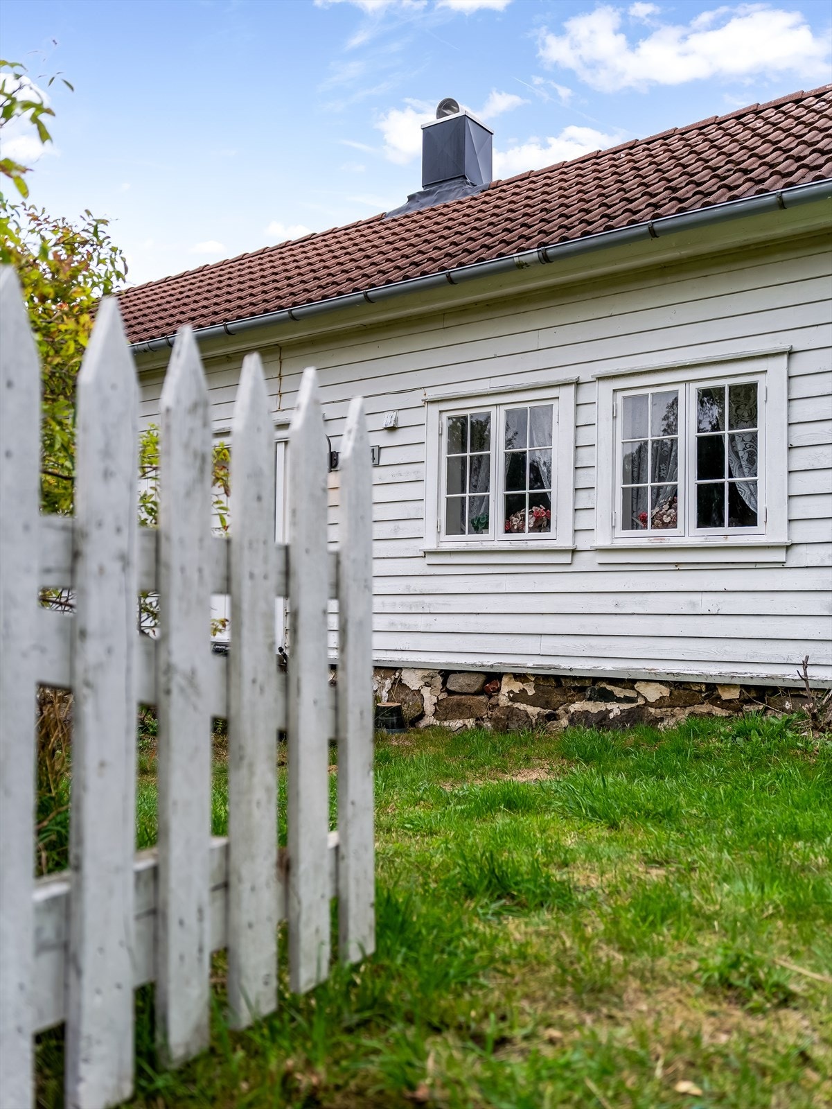 Hvit fasade med vinduer mot hagen - klassisk sørlandshus med steinsatt grunnmur. Galleribilde
