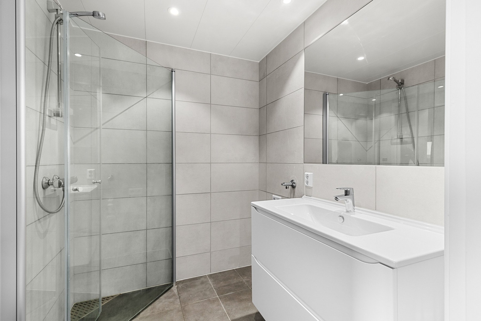 Praktisk bad med vegghengt wc, opplegg for vaskemaskin, servant, speil og dusj med innfellbare glassdører. Downlights i himling. Galleribilde