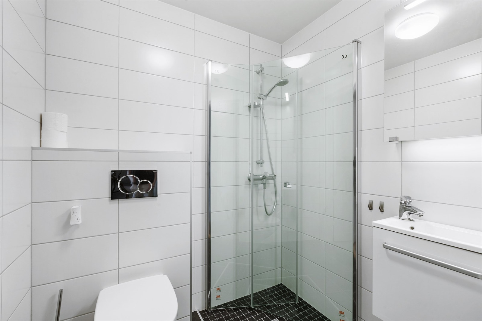 Flislagt bad med baderomsinnredning, vegghengt toalett og dusjhjørne Galleribilde