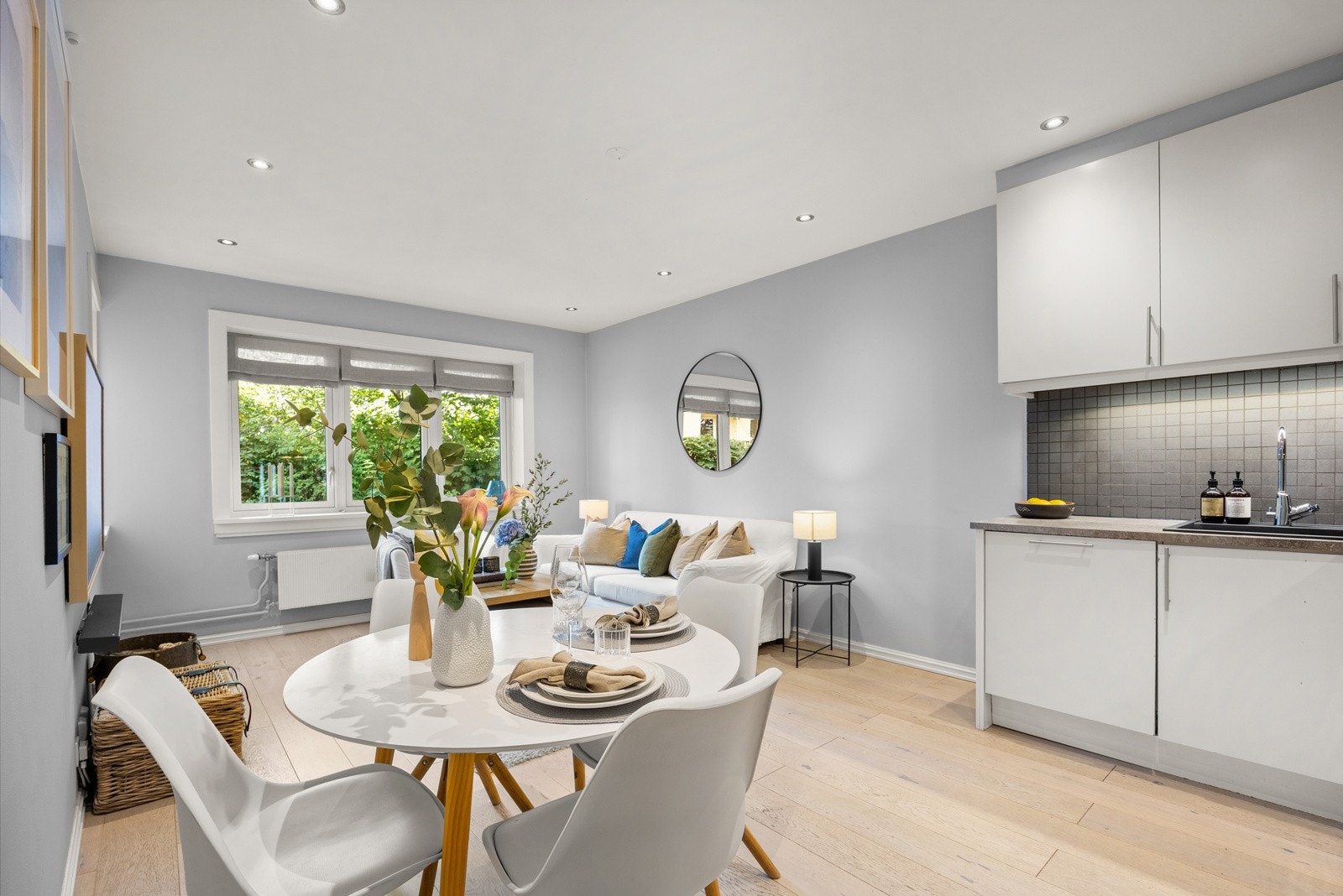 Atmosfæren i stuen preges av store vinduer i enden av rommet som vender mot grønne busker og trær. Galleribilde