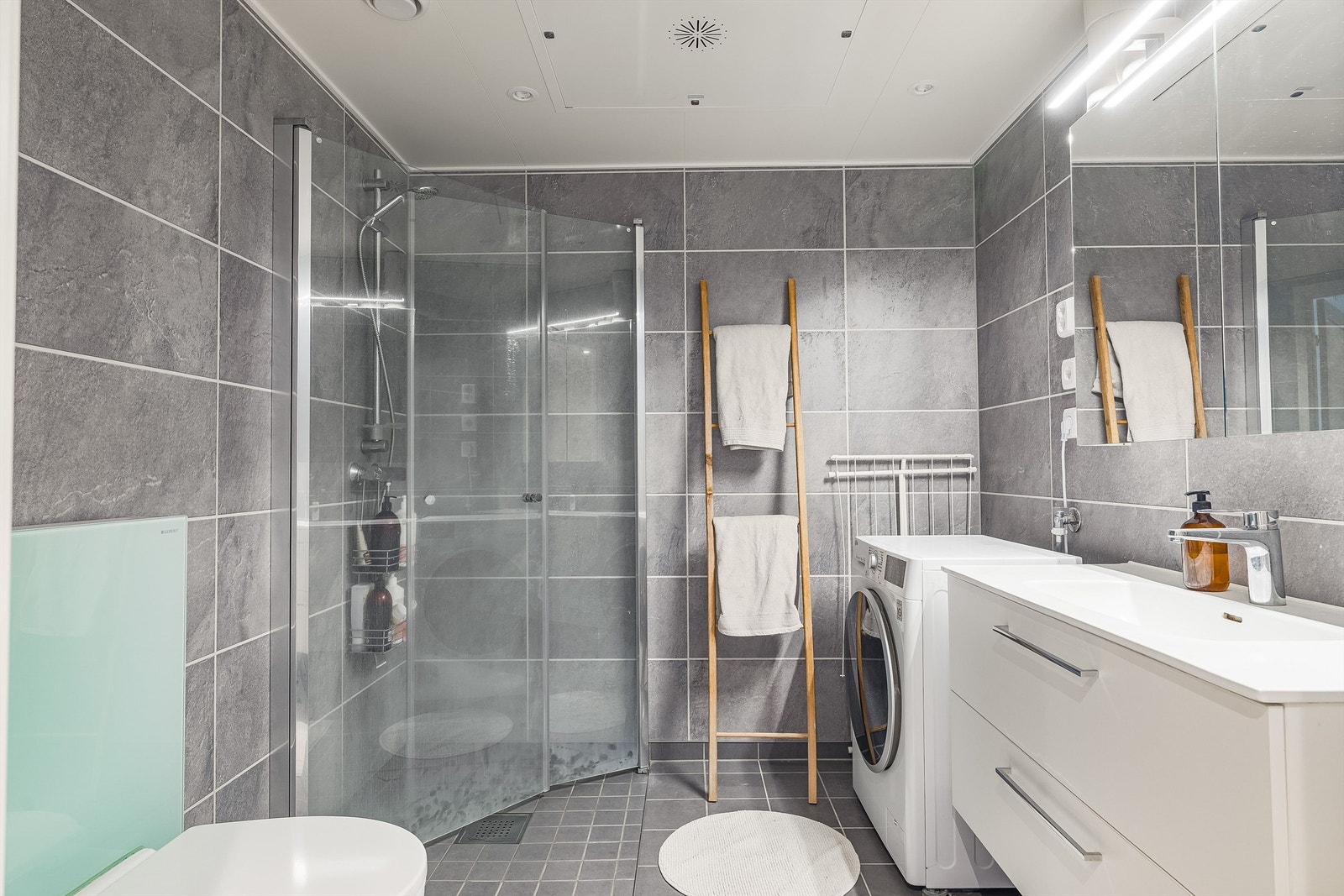 Moderne bad med flislagt gulv, vegghengt toalett og dusjhjørne med glassdører. Galleribilde