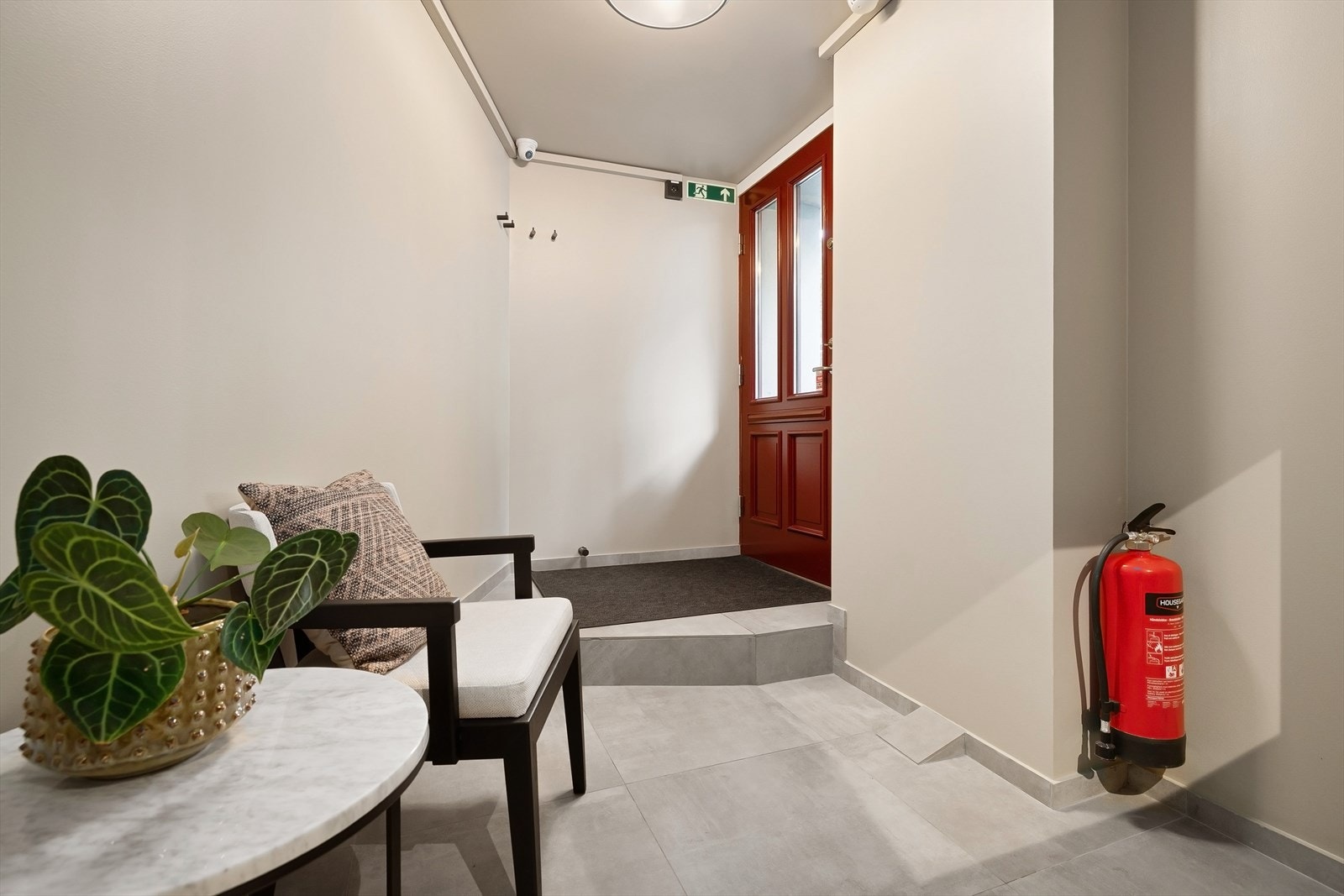 Lokalet har to innganger fra gateplan. Dette er den nederste inngangen. Her er det laget et lite inngangsparti med venterom og luke inn til en liten resepsjon. Døren her nede kan også åpnes og overvåkes fra den store resepsjonen i etasjen over. Galleribilde