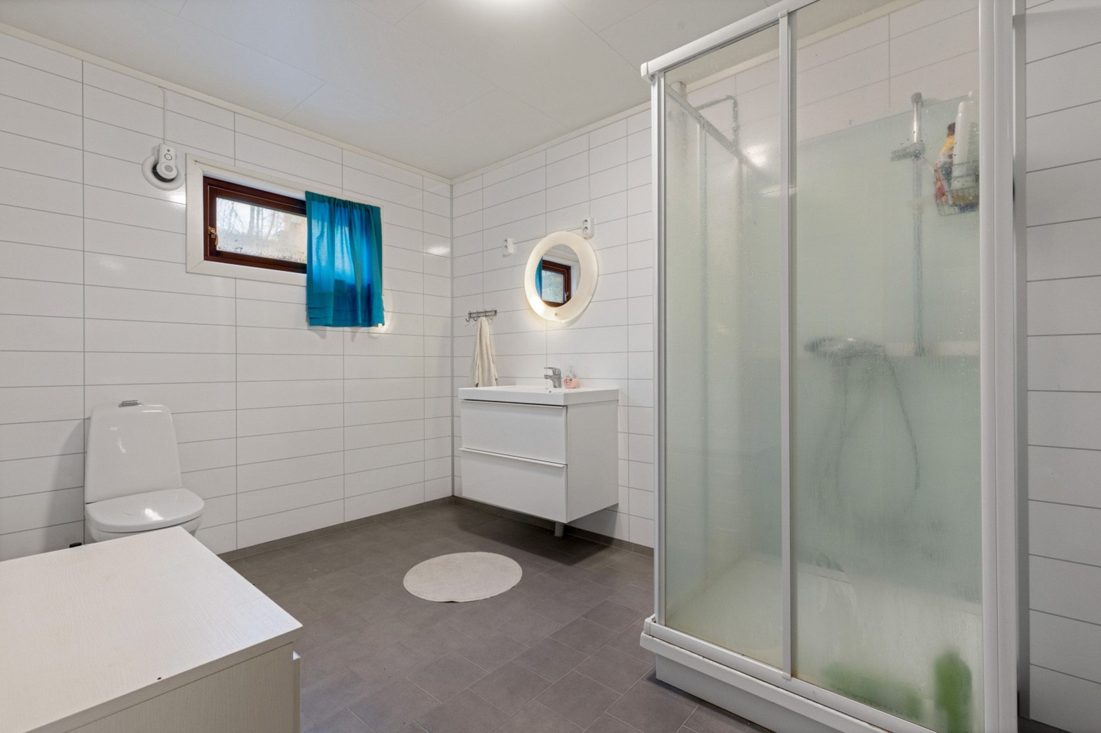 Romslig baderom som holder et tidløst preg og er bestående av servant med underskap. toalett og dusjkabinett Galleribilde