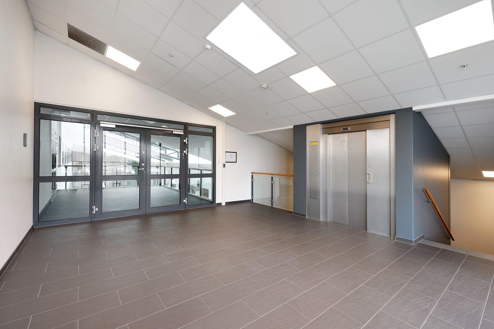 Moderne inngangsparti med heis og store glassdører. Lys og romslig atmosfære. Galleribilde