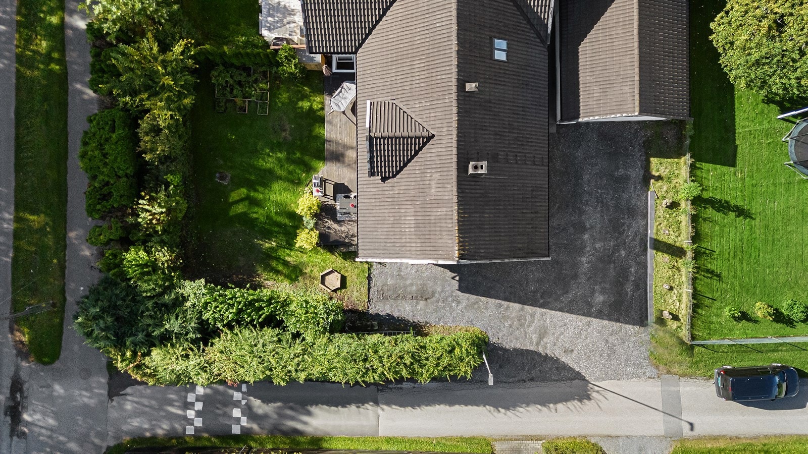 Gruset gårdsplass som deles med naboen. Boligen har utvendig biloppstillingsplass langs kortveggen og foran trappen mens nabo disponerer garasje og plassen foran. Galleribilde