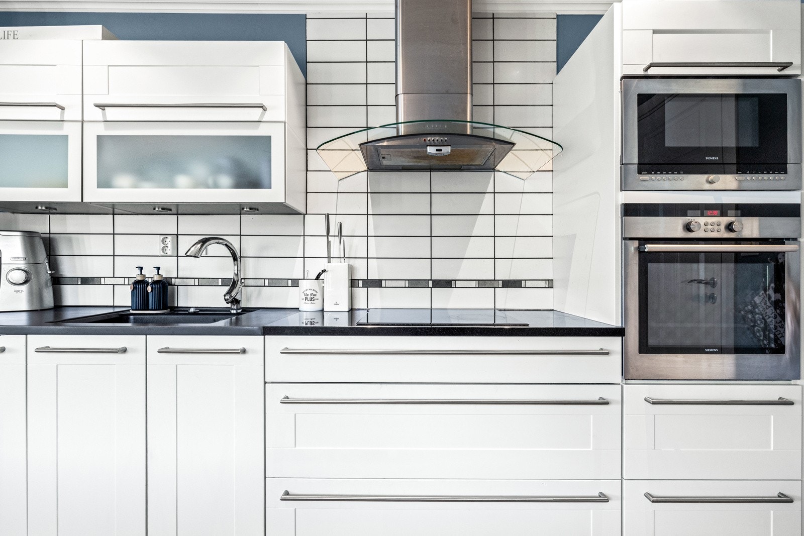 Kjøkkeninnredning fra Kvik med stein- og heltre benkeplate, håndtak i rustfritt stål og integrerte hvitevarer. Galleribilde