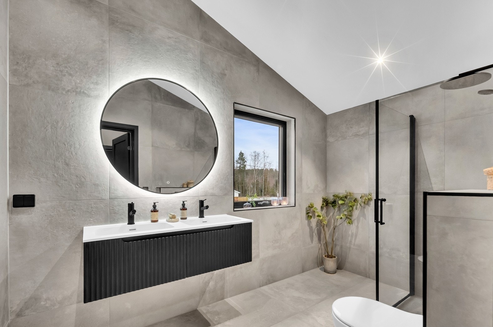 På badet oppe er det et rundt speil med bakenforliggende belysning og en stilig, sort skuffeinnredning med dobbel servant. Galleribilde