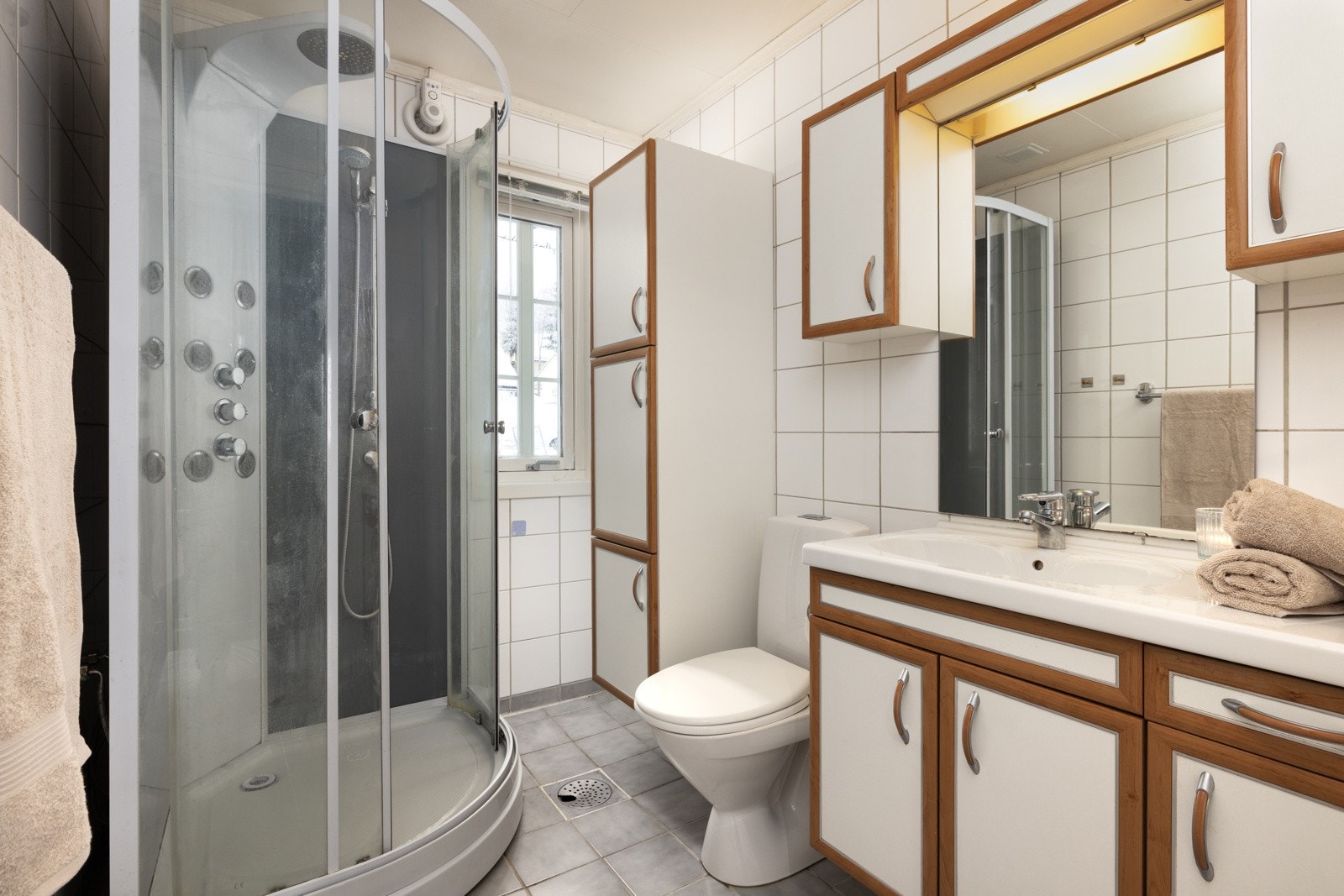 Lyst baderom med dusjkanbinett, hvite fliser og god oppbevaringsplass. Galleribilde