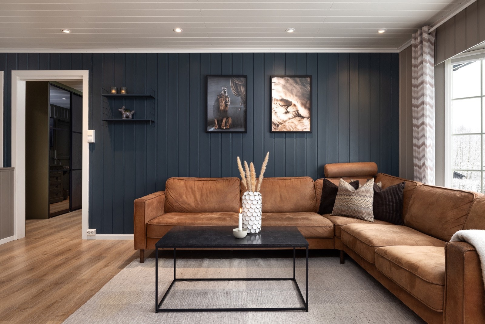 Koselig sofakrok med mørke blå panelvegg og store vinduer som slipper inn med naturlig lys. Galleribilde