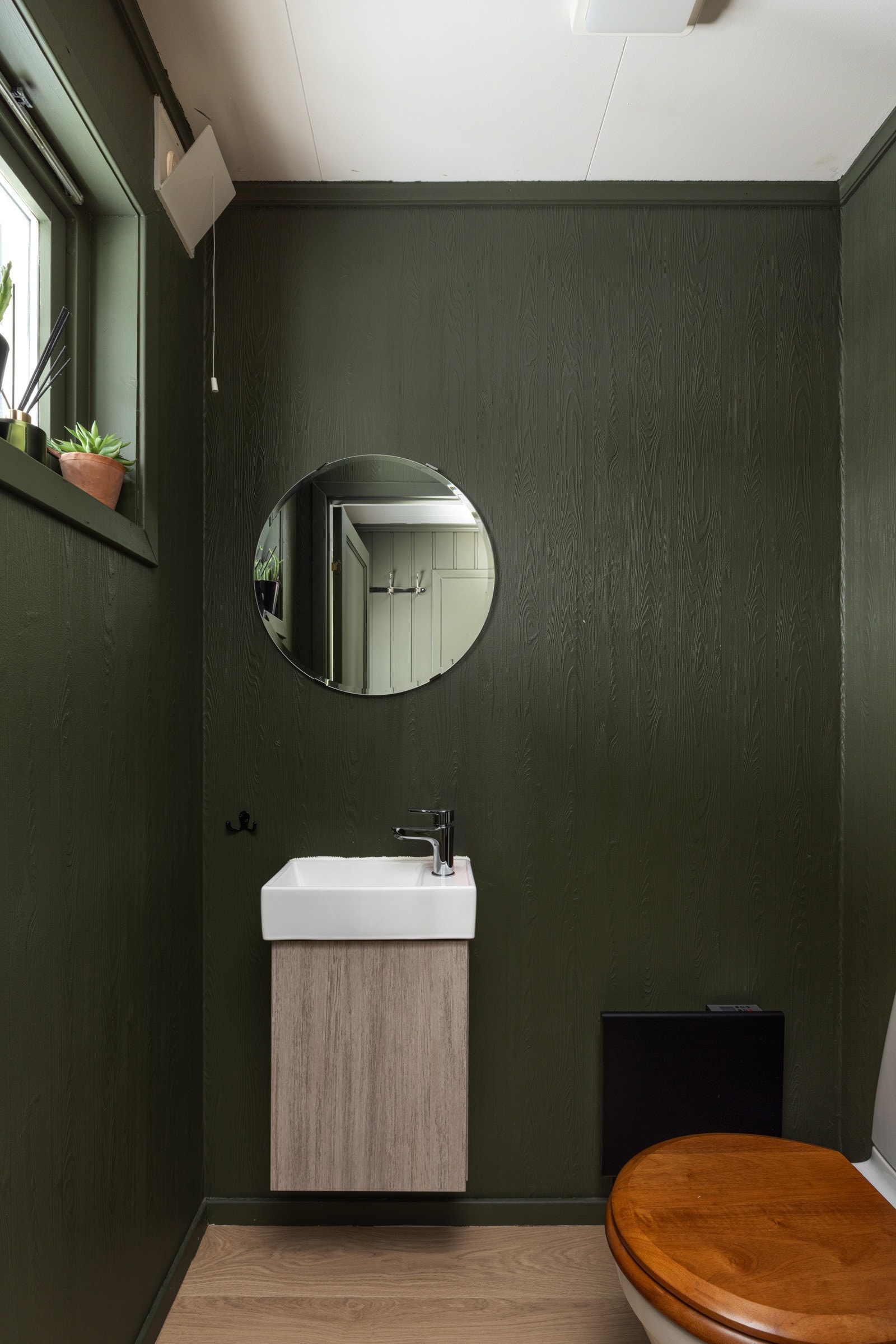 Toalettrom med mørkegrønne vegger og kompakt servant. Galleribilde