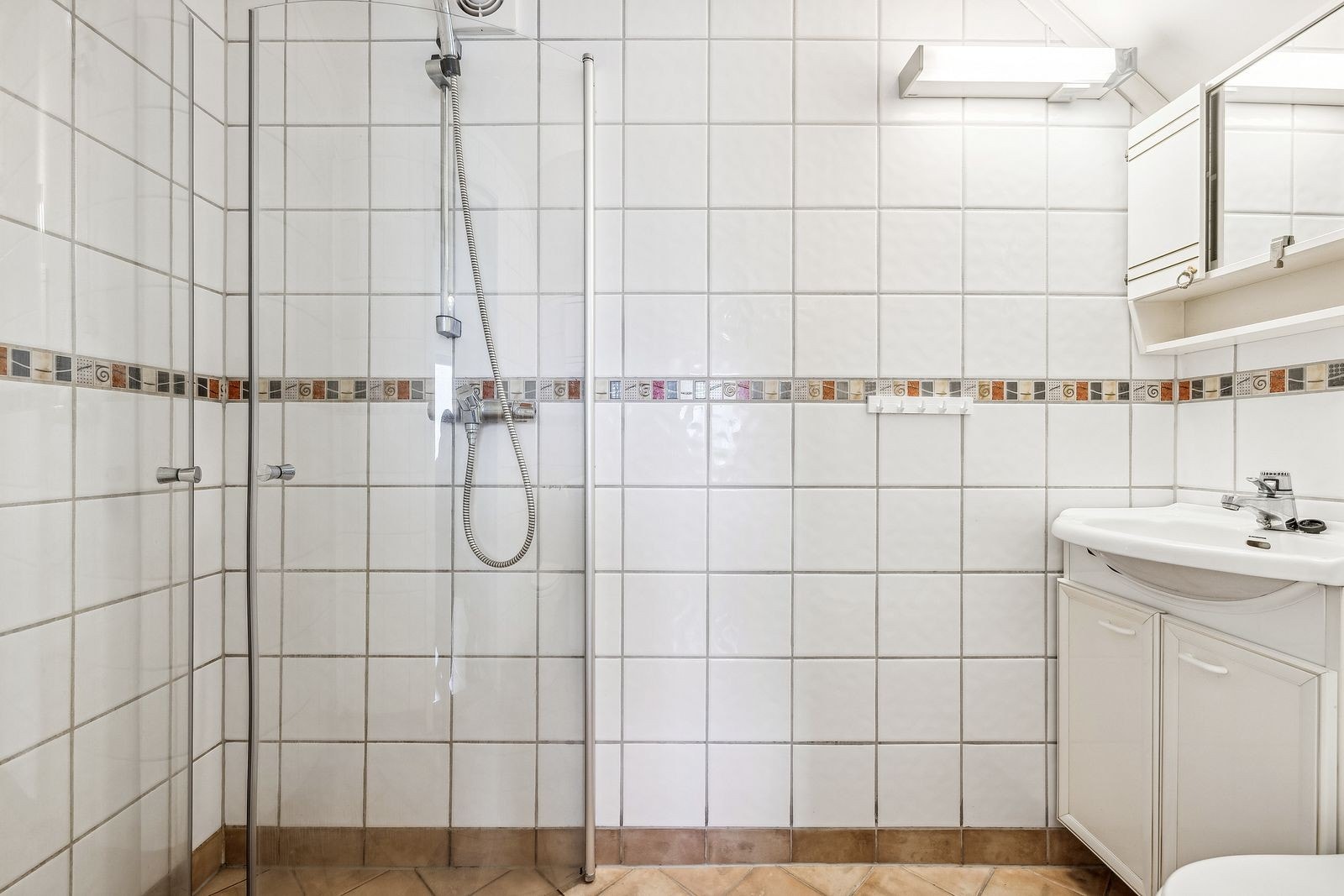 Flislagt baderom med dusj, toalett, speilskap og ytterligere baderomsinnredning. Galleribilde