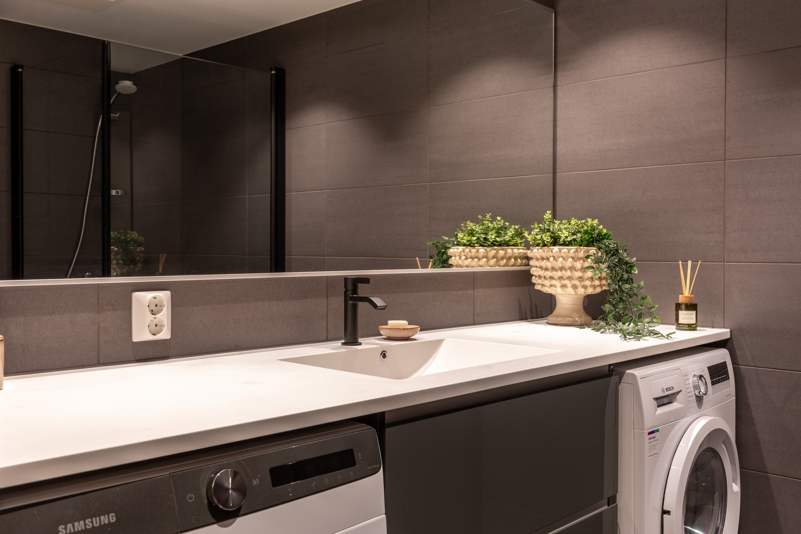 Badet er innredet med vegghengt servantskap med heldekkende servant, speil med overlys på vegg over servant, dusjnisje med innfellbare glassdører og dusjarmatur, samt vegghengt toalett. Galleribilde