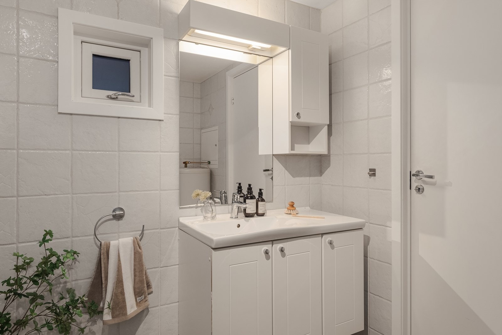 Baderommet er innredet med veggmontert toalett, servant med møbler, dusjvegg, varmtvannstank og opplegg for vaskemaskin. Det er mekanisk avtrekk og tilluft via spalte under dør. Galleribilde