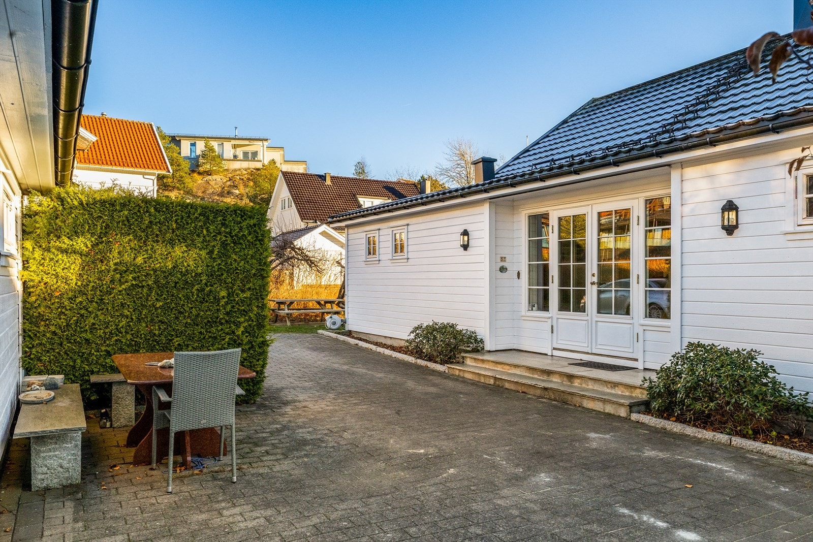 På inngangssiden har boligen en gårdsplass med blomsterbed og belegningsstein. Galleribilde