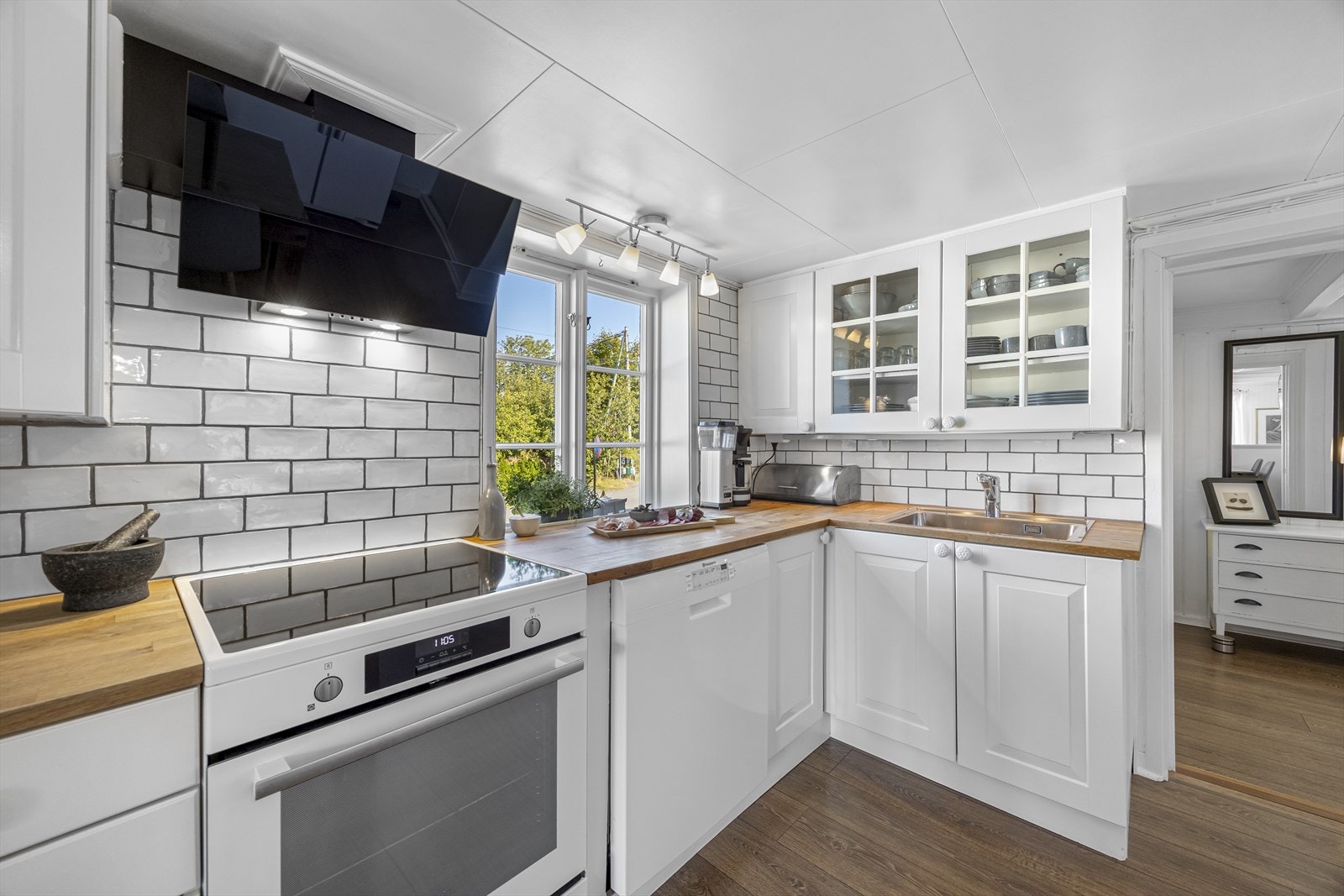 Lys og pent kjøkken med fliser og kjøkkenbenk og trebenkeplate. Galleribilde