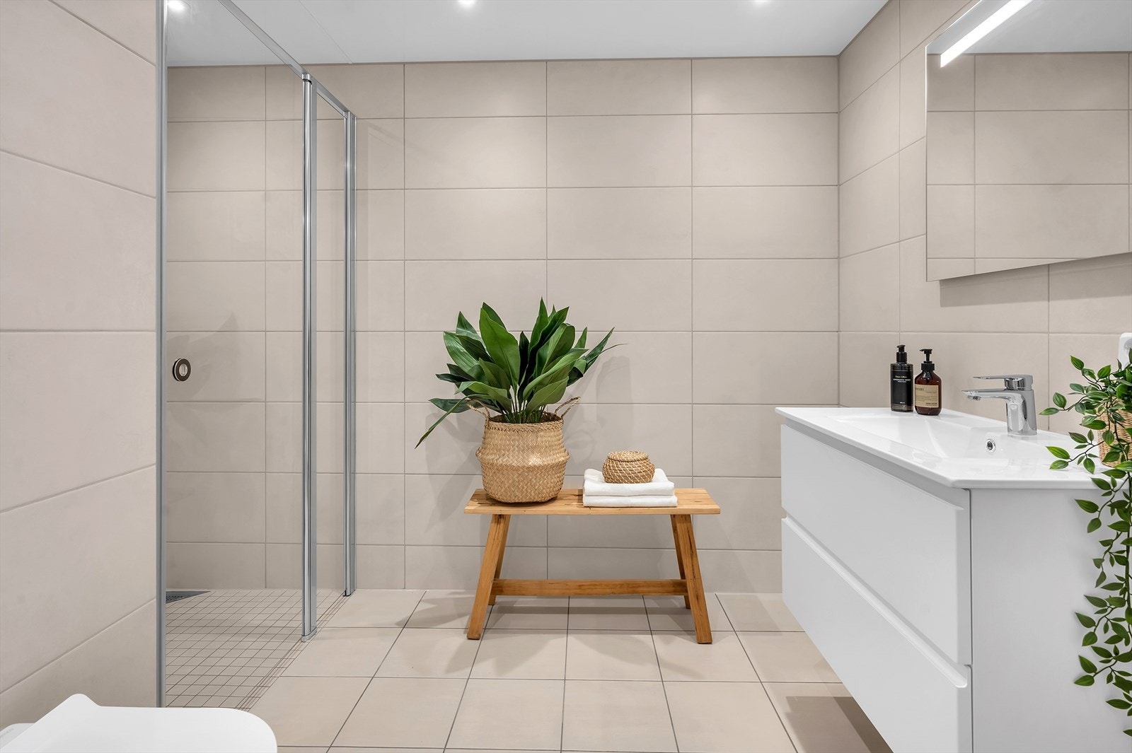 Flislagt baderom med vannbåren varme i gulvet. Badet er utstyrt med baderomsmøbel med servant, dusjnisje og vegghengt toalett. Galleribilde