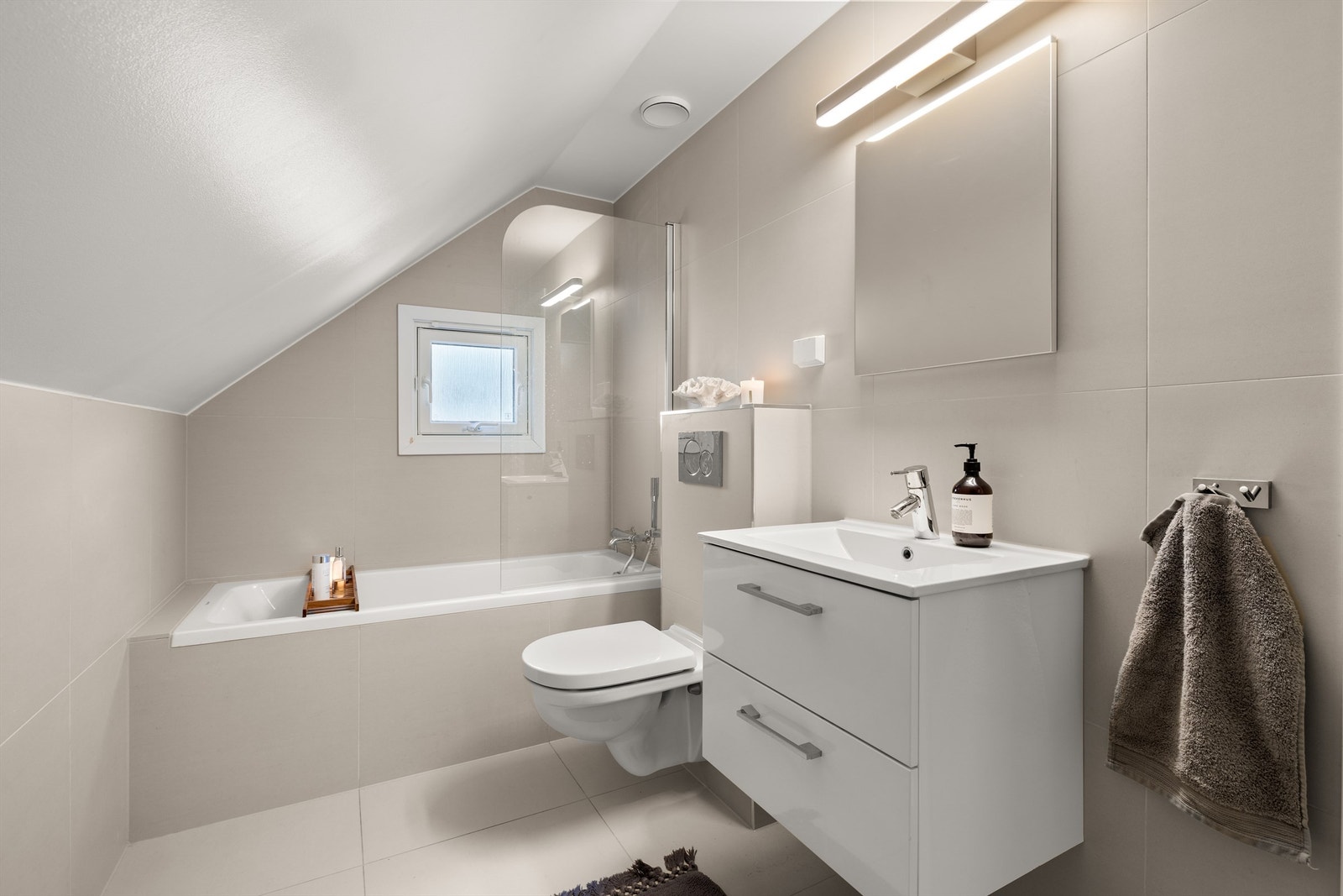 Badet på loftet ble oppgradert i 2019 med flis på flis, og har innbygget badekar med dusjvegg, vegghengt toalett og servantinnredning Galleribilde