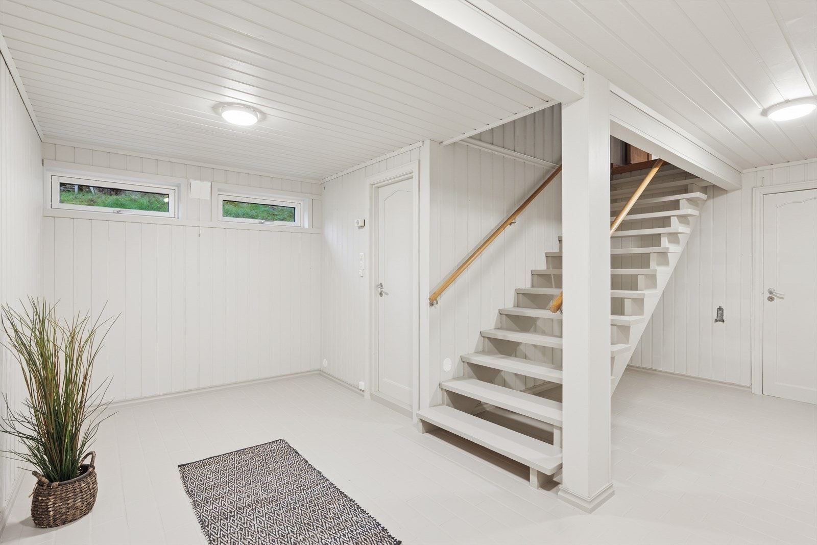 Lys og romslig hall i underetasje med trapp til hovedplan, lyse vegger og vinduer som gir naturlig lys Galleribilde