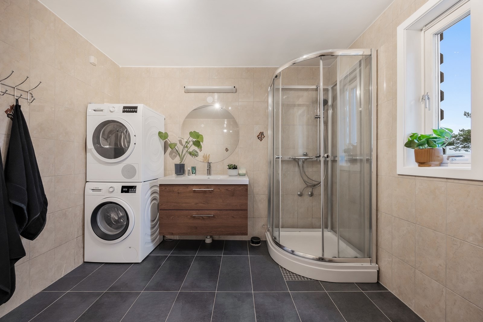 Baderommet inneholder dusjkabinett, servantseksjon med skuffer, vegghengt speil, gulvmontert klosett og opplegg for vaskemaskin/tørketrommel. Galleribilde