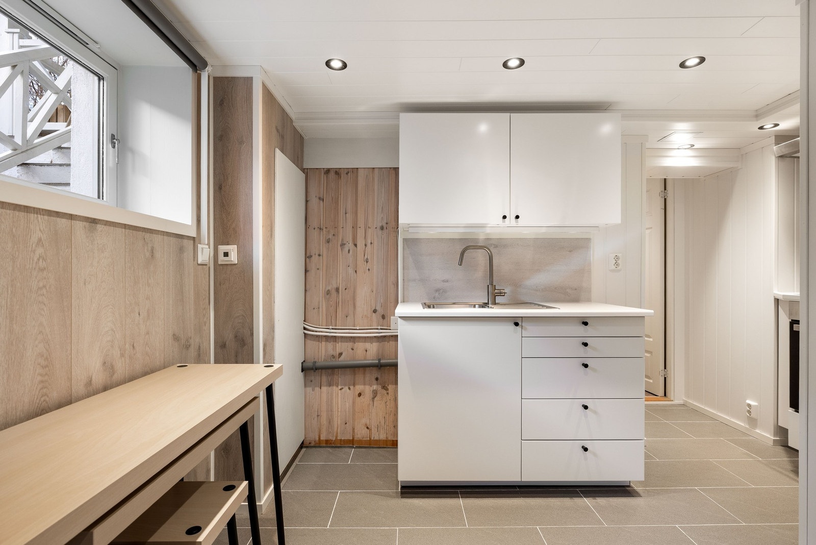 Rom i kjeller som er innredet med enkel kjøkkenbenk og skap. Galleribilde