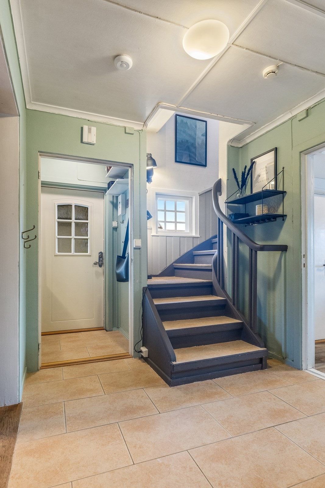 Luftig entré med flis på gulv, malt strietapet på vegg og panelplater i himling med listverk. Galleribilde