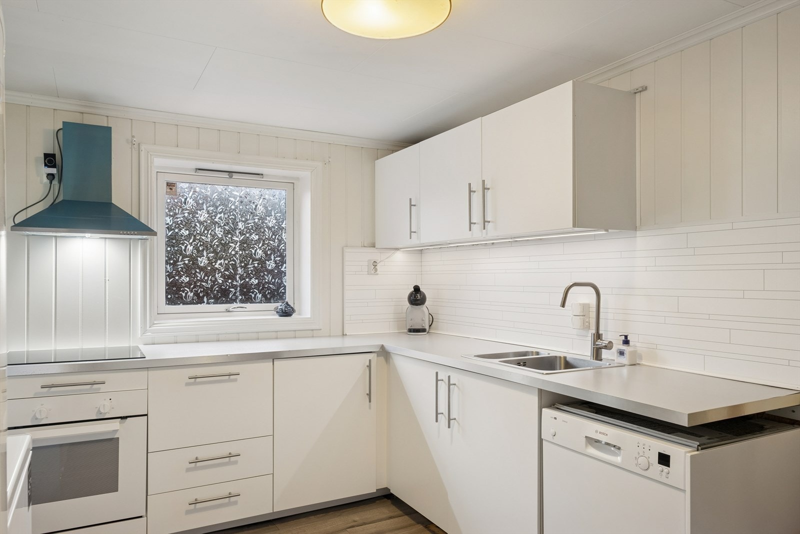 Kjøkkenet er med lyse slette fronter, laminert benkeplate og oppvaskkum. Kjøkkenet er utstyrt med oppvaskmaskin, komfyr, induksjonstopp og avtrekksvifte. Galleribilde