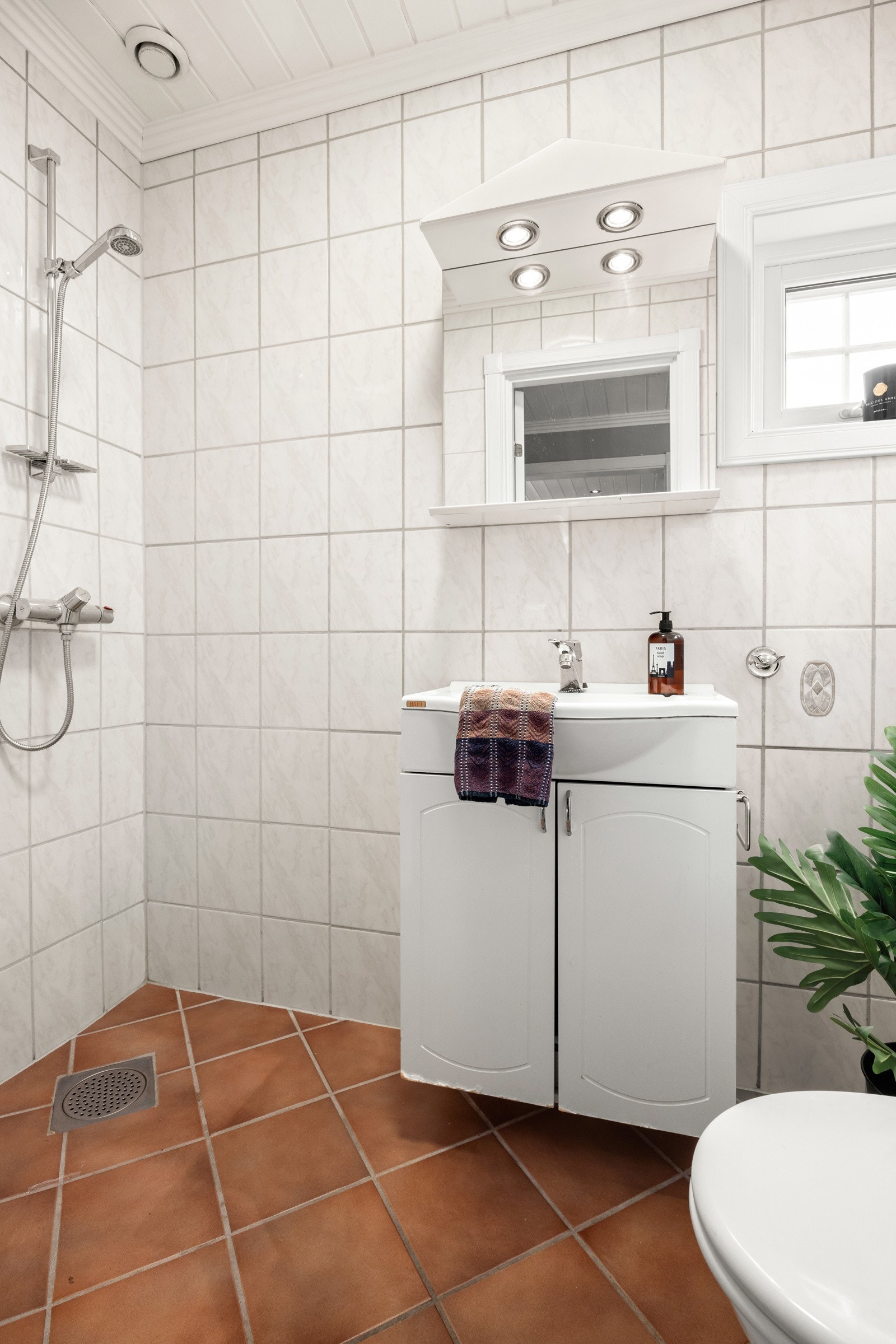 Flislagt bad utstyrt med toalett, dusj, servant integrert i skapinnredning og speihylle med lys Galleribilde