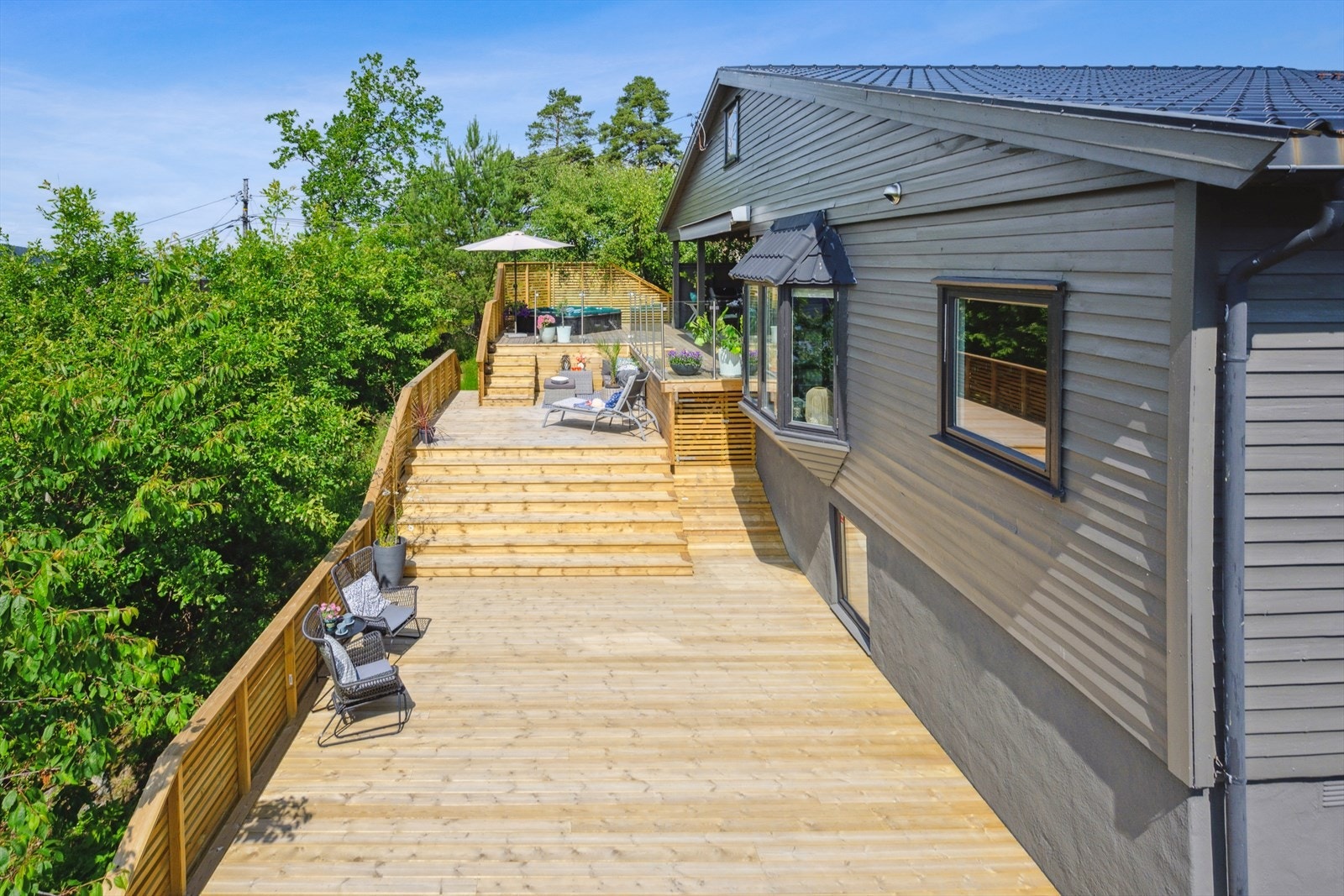 Tiltalende terrasse fra 2025 med dekke av tre og rekkverk av liggende trepanel. Herlig skjermet terrasse med markise, delvis overbygg med belysning i tak/vegger. Galleribilde