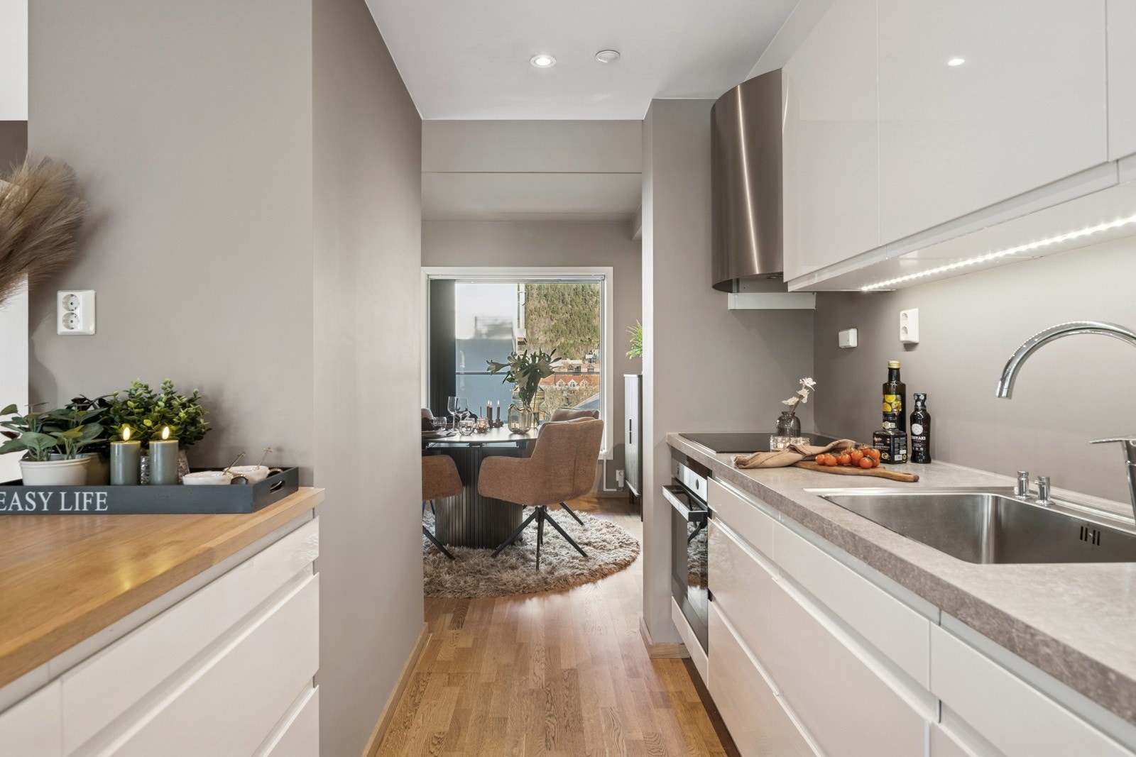 Lys og moderne kjøkkenløsning med godt med benkeplass og naturlig gjennomlys mot spiseområdet. Galleribilde