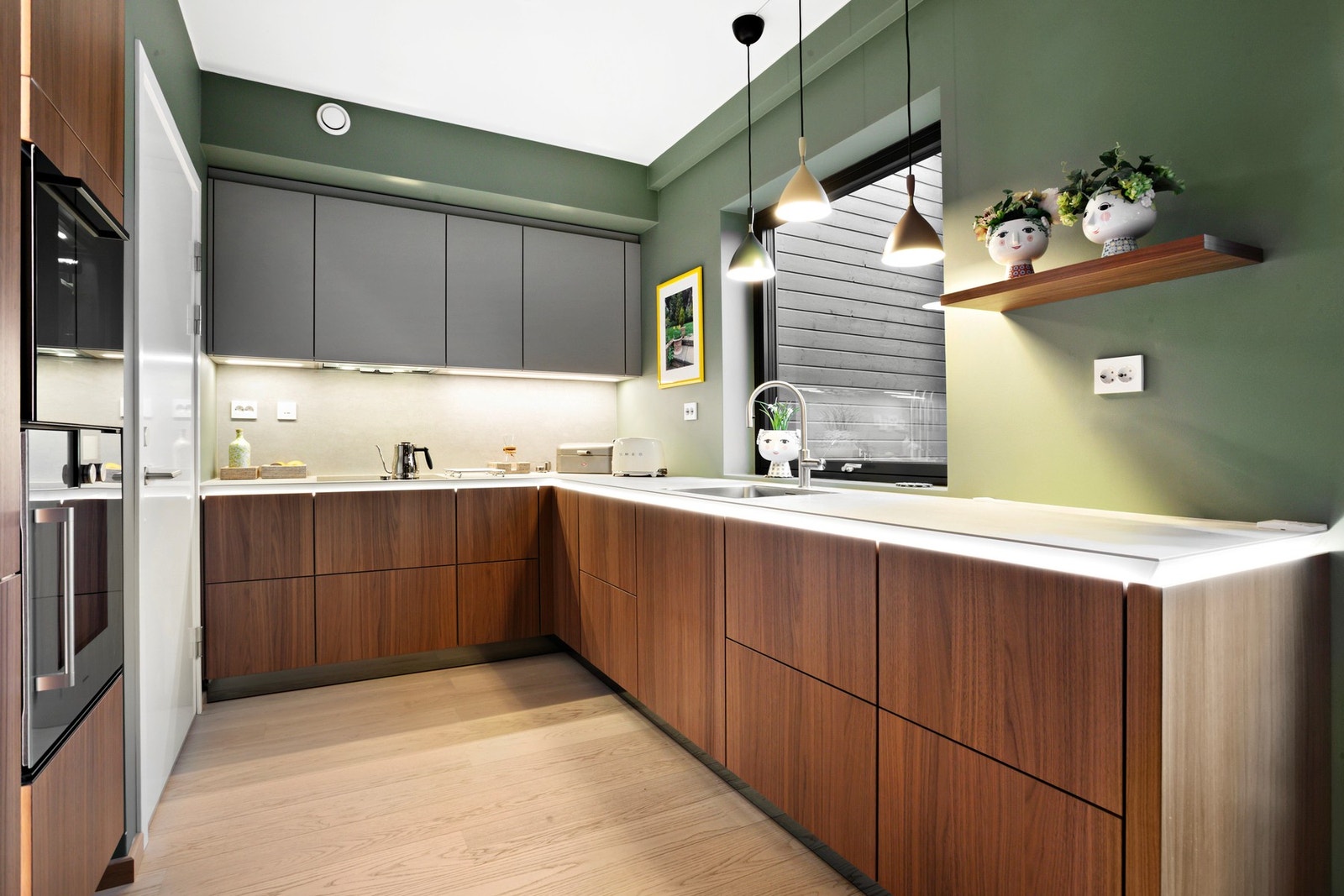 Et moderne og stilrent kjøkken med varme trefronter, grønne vegger og elegant belysning som skaper en lun atmosfære. Galleribilde
