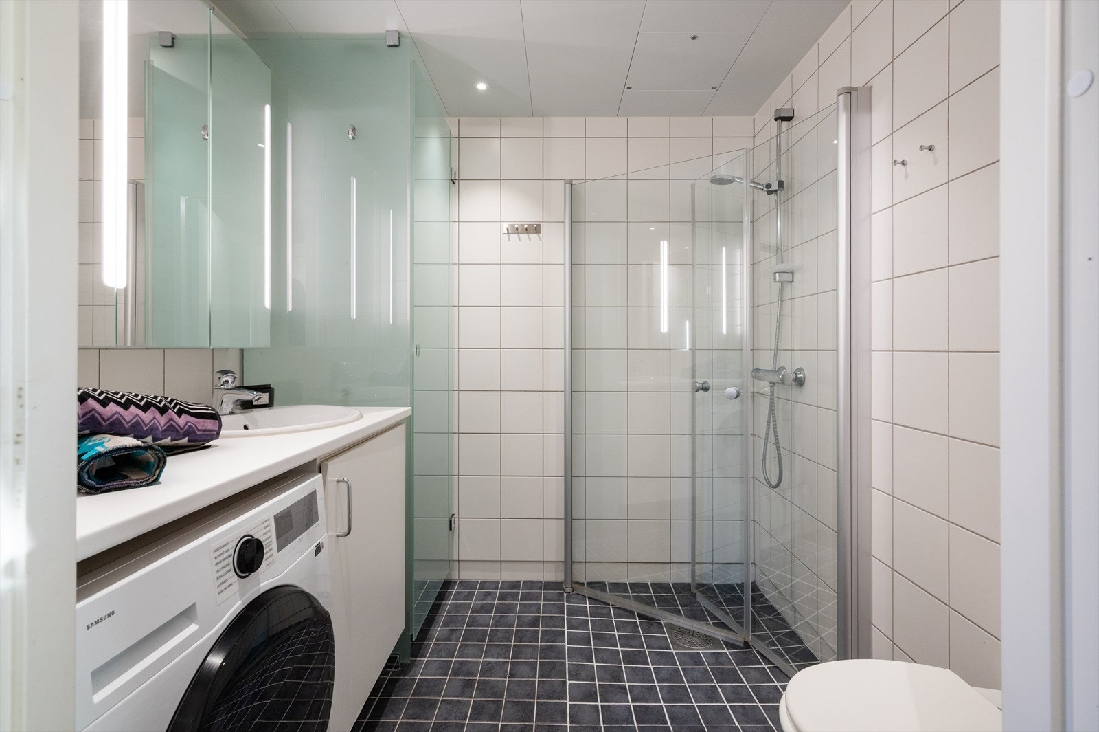 Moderne og flislagt bad med innfellbare dusjdører, gulvvarme og downlight i tak. Galleribilde